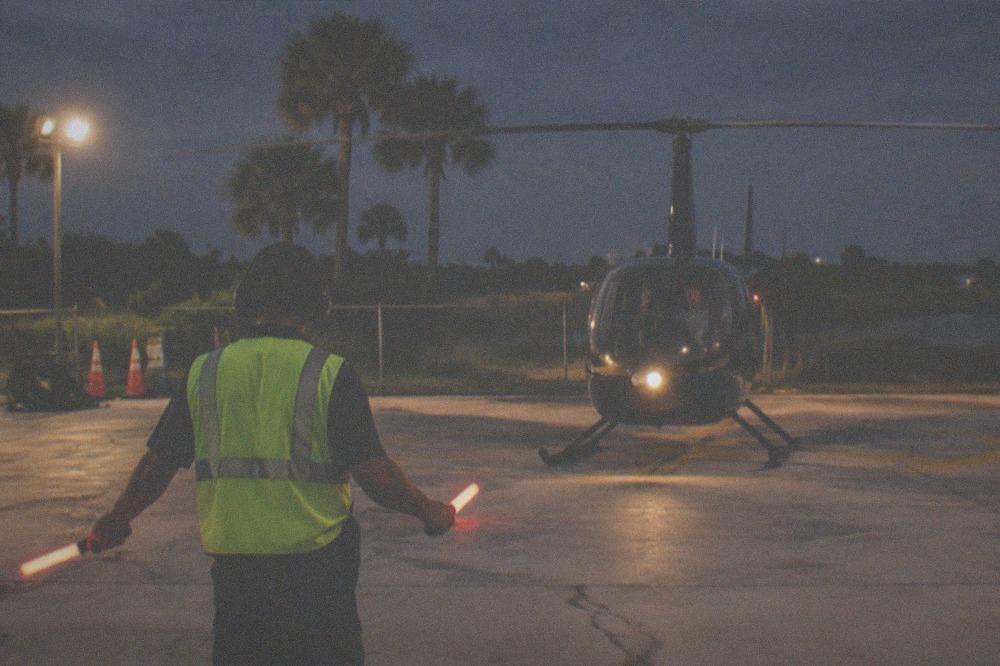 Helicopter on a lit helipad at night with ground crew preparing for a flight