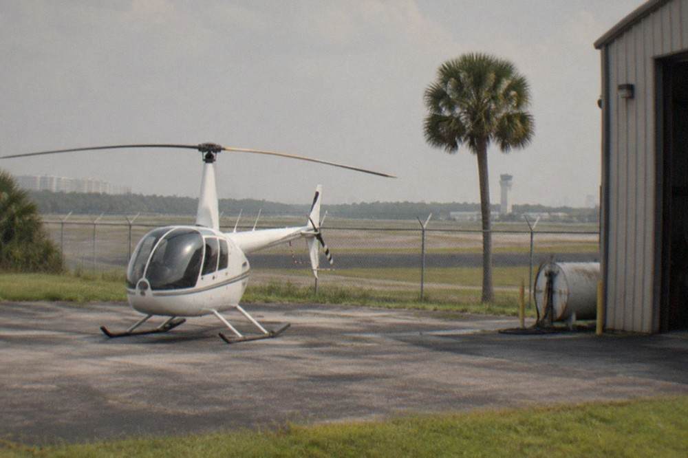 Small tour helicopter on a paved helipad beside a fenced airfield in Kissimmee