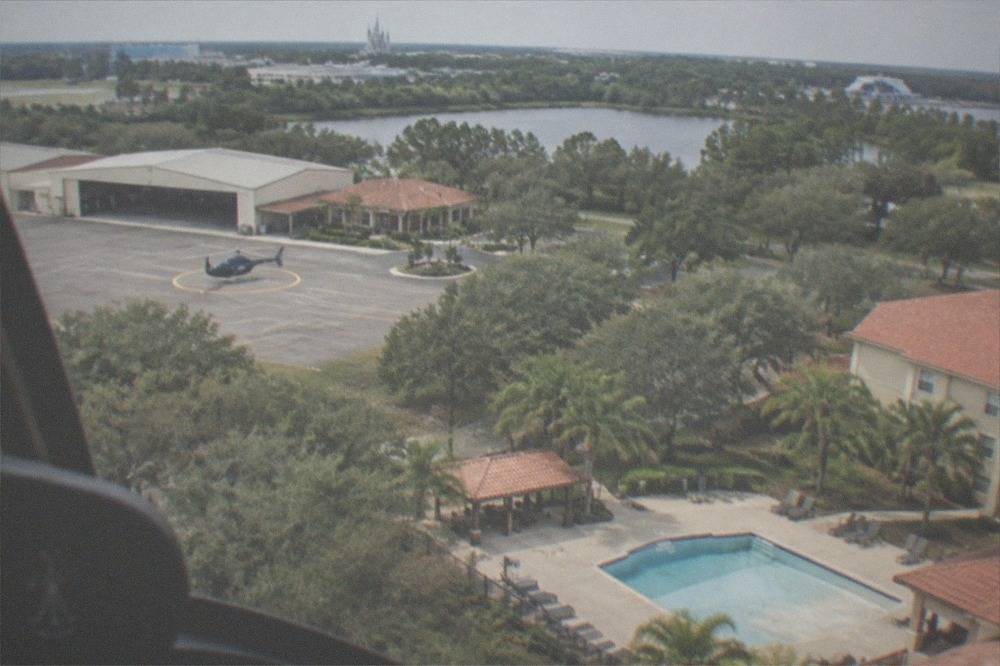 A light tour helicopter flying above resort rooftops and tree lines in the Lake Buena Vista area