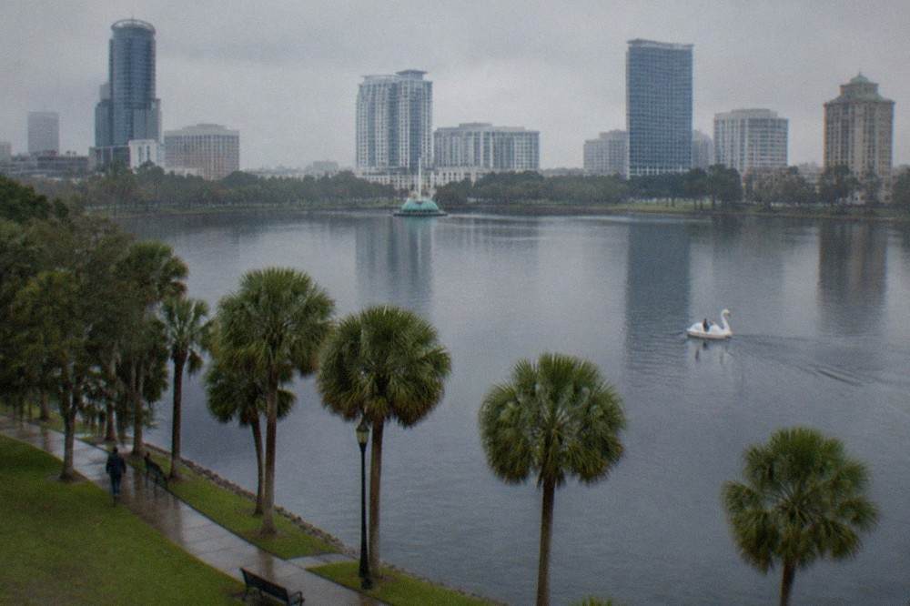 Wide aerial view of a lakefront park surrounded by city buildings and palm trees