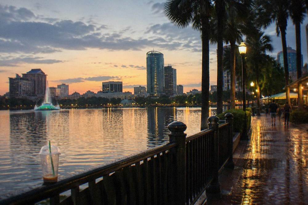 Evening view of a lit waterfront promenade with shops and palm trees