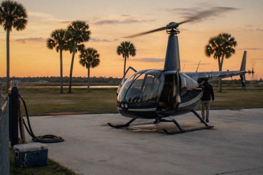 A small helicopter on a helipad at dusk with the cabin door open and rotor blades still turning