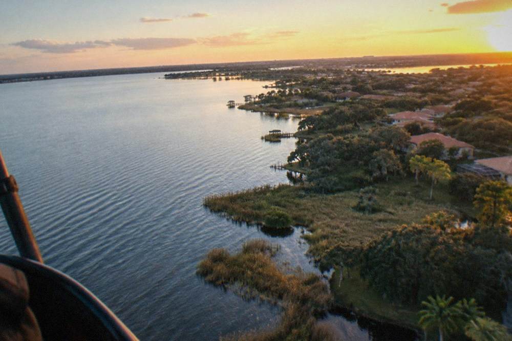 Aerial view across a large Florida lake at golden hour with tree lines and distant suburban rooftops