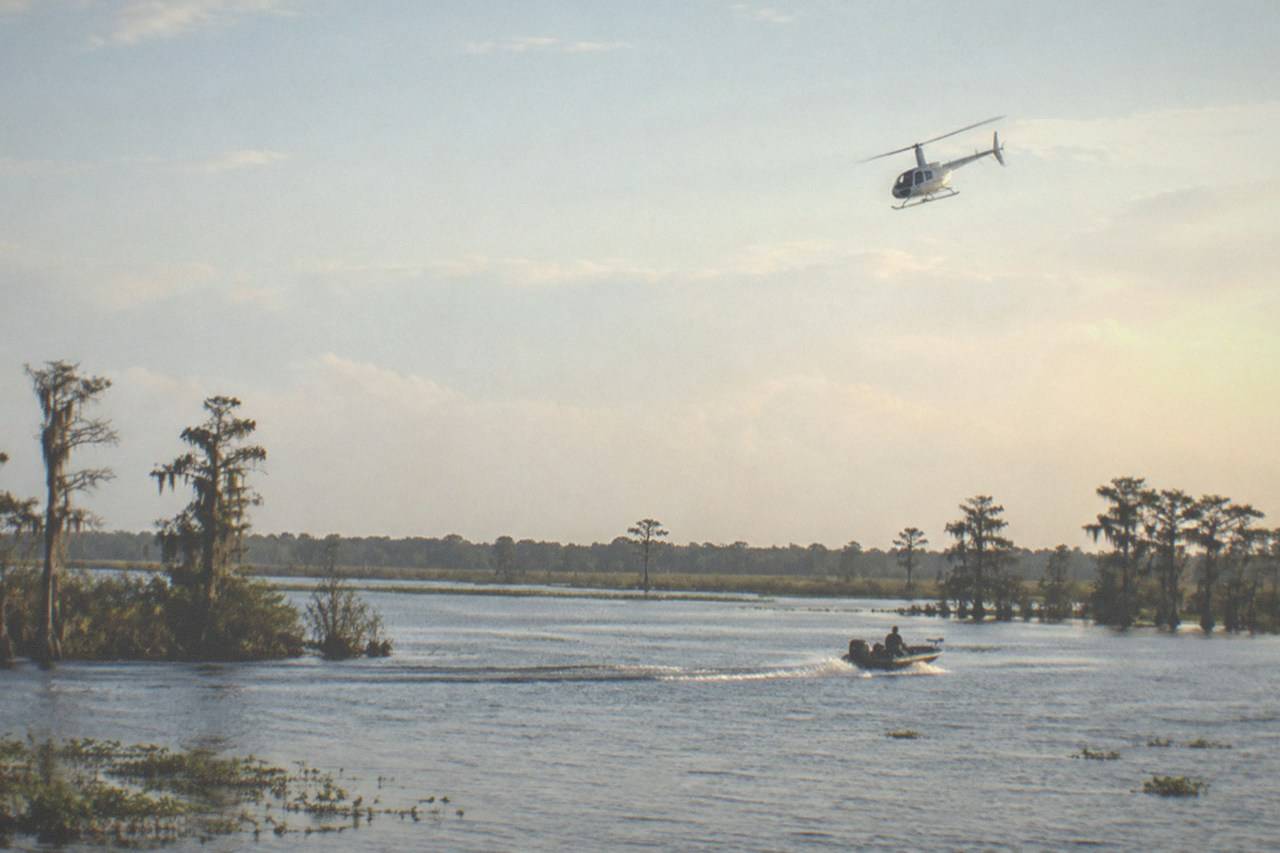 Wide establishing view. A small sightseeing helicopter turning above the lake-sprinkled flatlands around Kissimmee in afternoon light, framed against broad open sky, no people, no logos, no readable text.